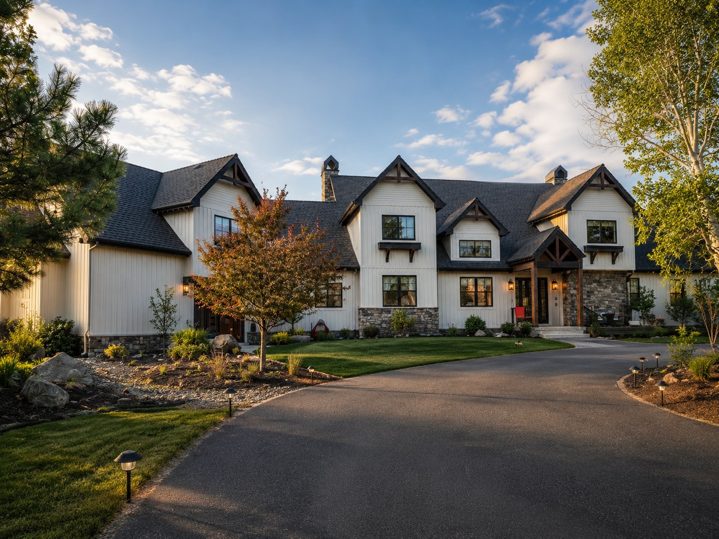 Private acreage home in Bend Oregon — white board and batten siding, dark timber brackets, stone base, multi-gabled roofline, paver driveway, and mature landscaping — LT Northwest Builders