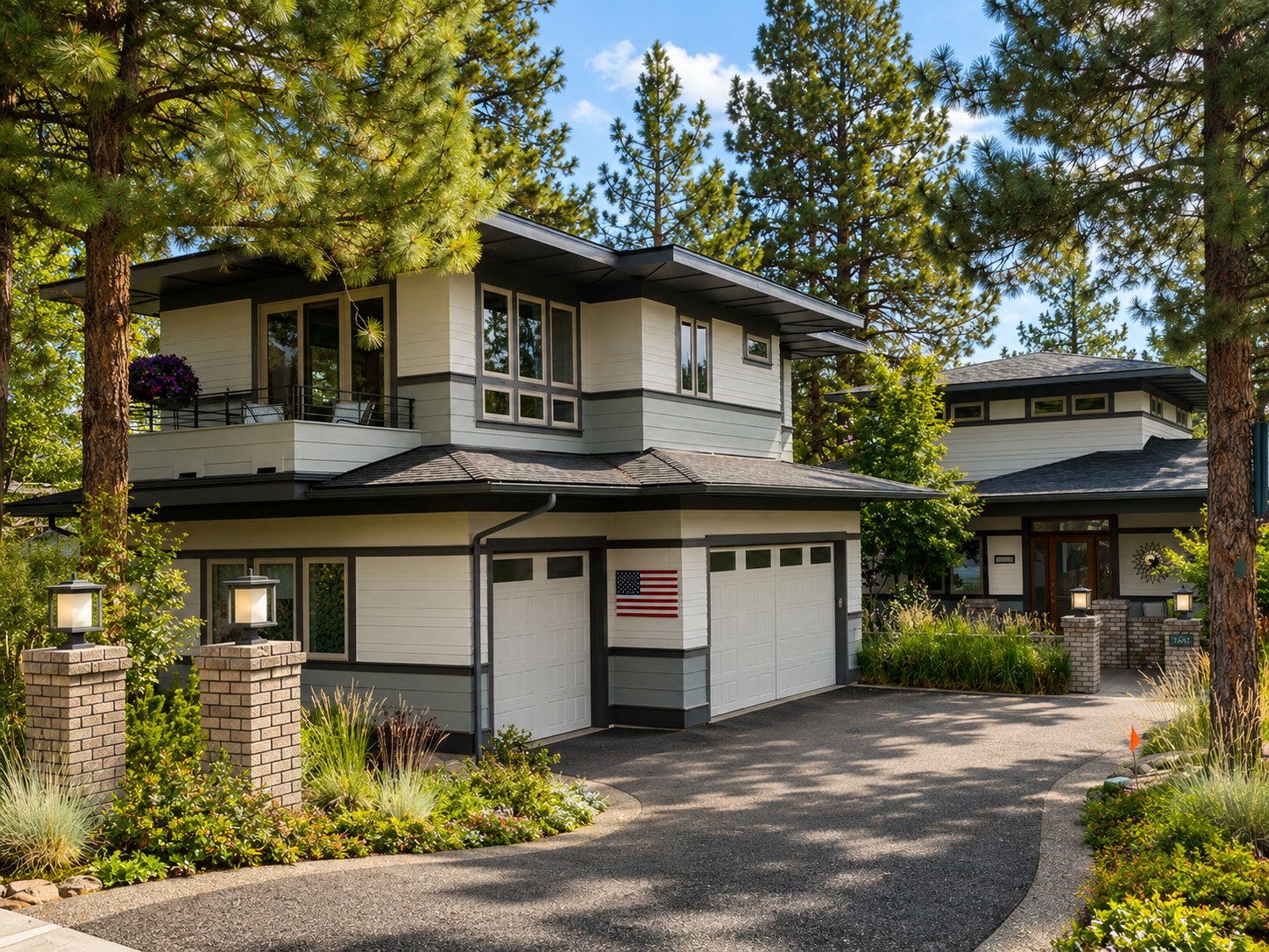 Custom designed and built garage ADU addition on Bend Oregon west side by LT Northwest Builders — two-story modern prairie-style architecture seamlessly integrated with existing home, upper-level deck with railing, clerestory windows, white horizontal siding with dark trim, brick entry columns, and mature ponderosa pine setting