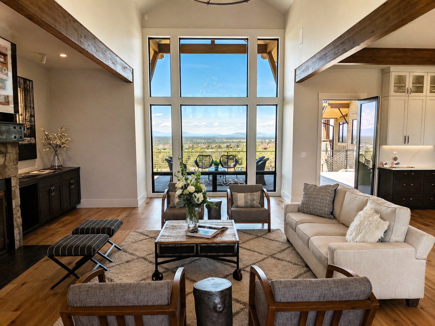 Brasada Ranch custom home great room — two-story black-framed windows with panoramic Cascade mountain and Bend views, exposed wood beams, stone fireplace, hardwood floors — LT Northwest Builders