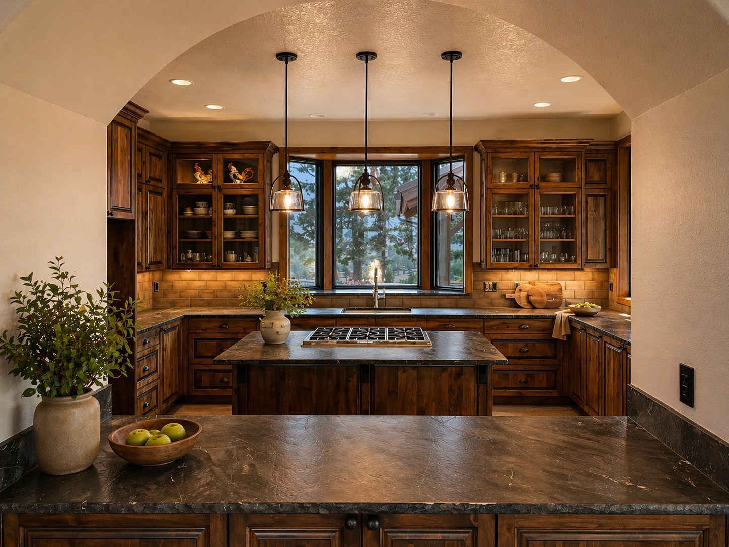 Custom kitchen in a Central Oregon working ranch home built by LT Northwest Builders — leathered stone countertops, knotty alder custom cabinetry, arched plaster entry, triple pendant lights over gas cooktop island, under-cabinet lighting, and ponderosa pine views through black-framed windows