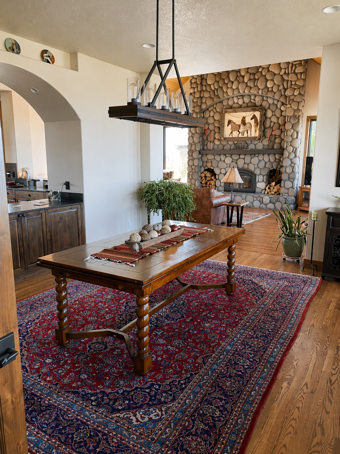 Open-plan dining and great room with river rock fireplace, barley twist dining table, Persian rug, and hardwood floors — Griffin Residence, Prineville Oregon