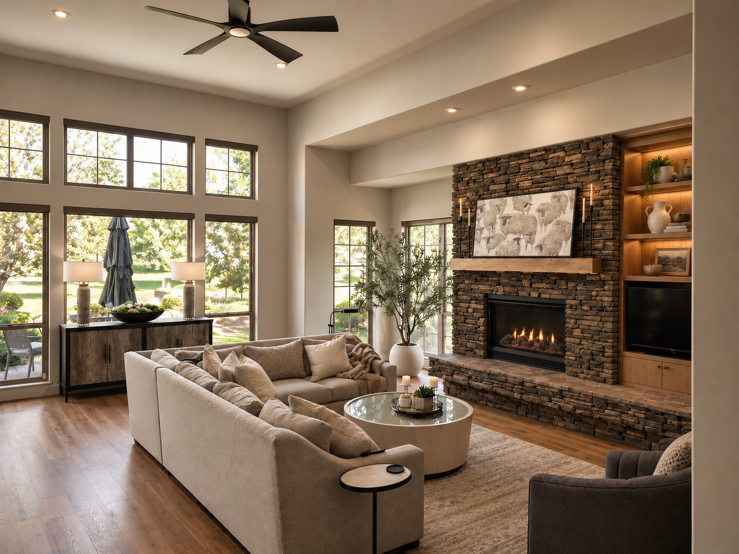 Reworked great room at Eagle Crest Golf Course — stacked stone fireplace with gas fire, built-in walnut shelving, large grid windows, sectional sofa, ceiling fan, and hardwood floors — Seek Residence, Redmond Oregon